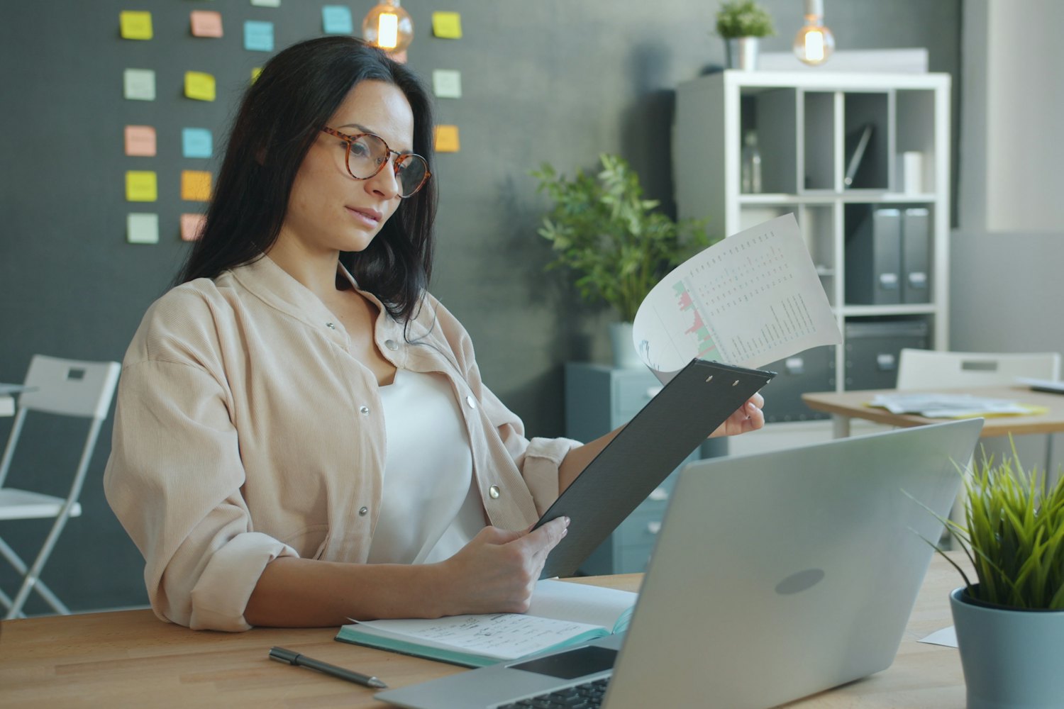 A professional reviews documents at her desk, with a planning wall behind her.