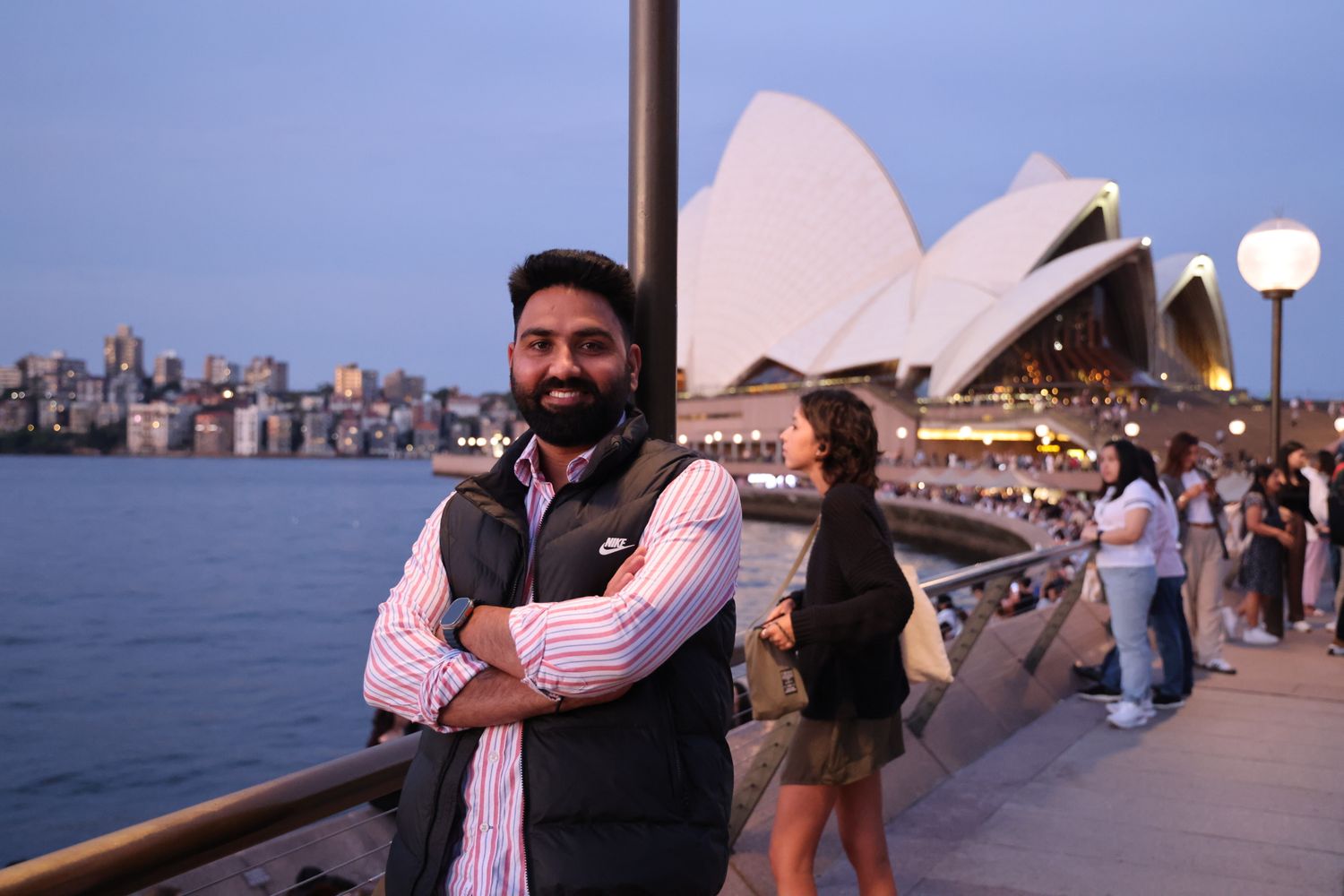 A man smiles by the Sydney Opera House at dusk.
